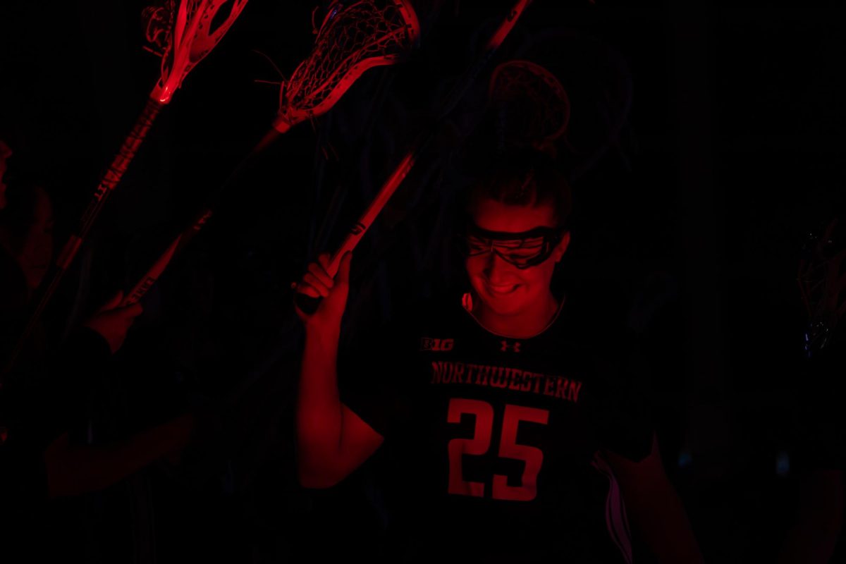 A player in a purple jersey runs under lacrosse sticks with a red light shining on them.
