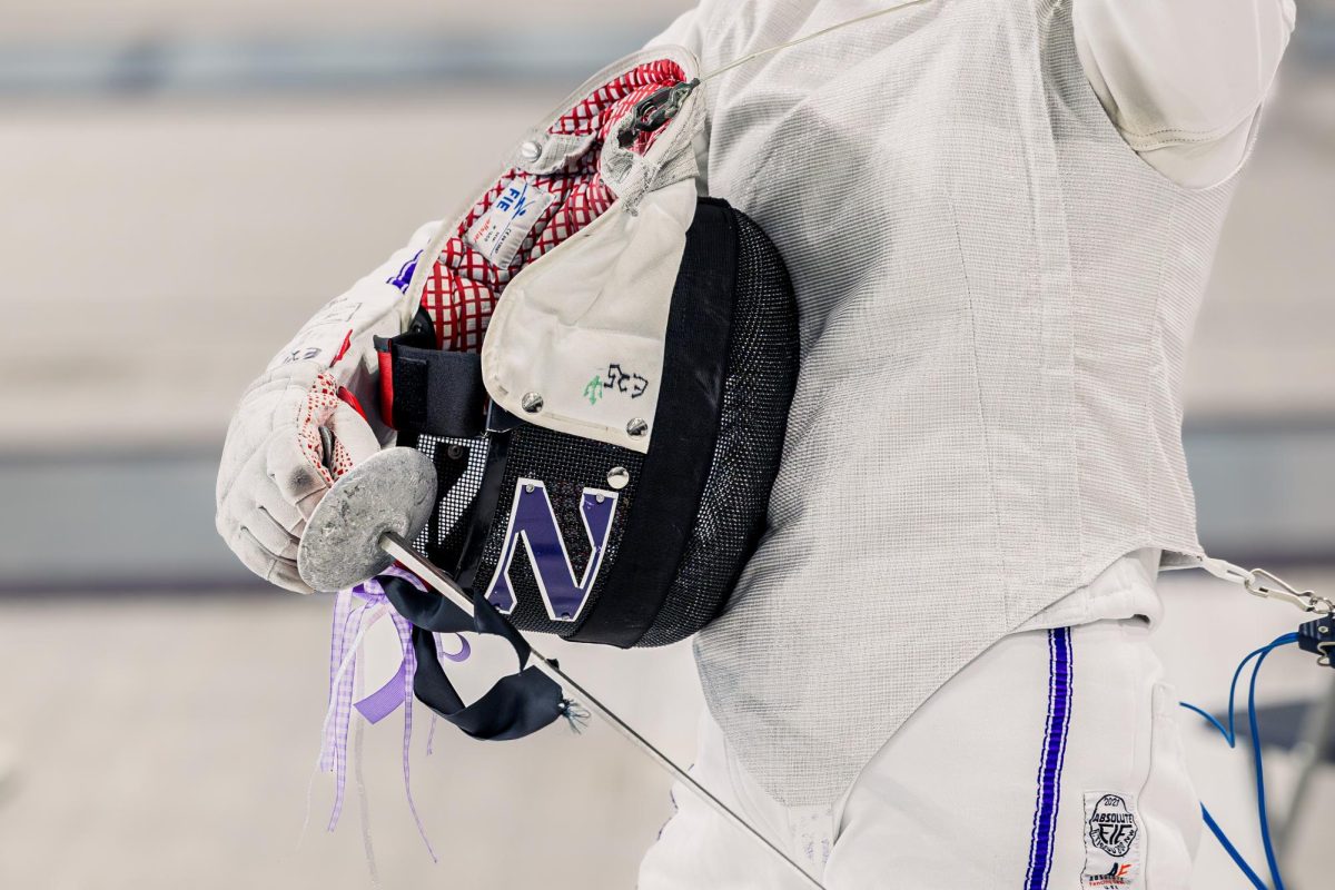 A Northwestern fencer holds their helmet and foil.