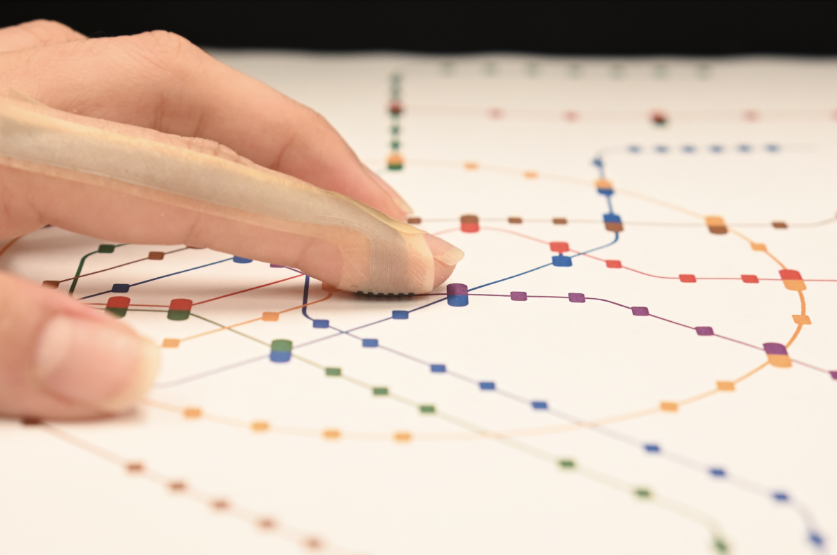 A finger with a bandage-like device with electric nodes touches a printed array of line segments
