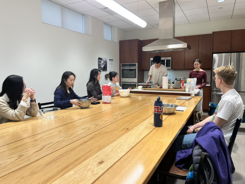 People sit around a table with various ingredients and kitchen tools.