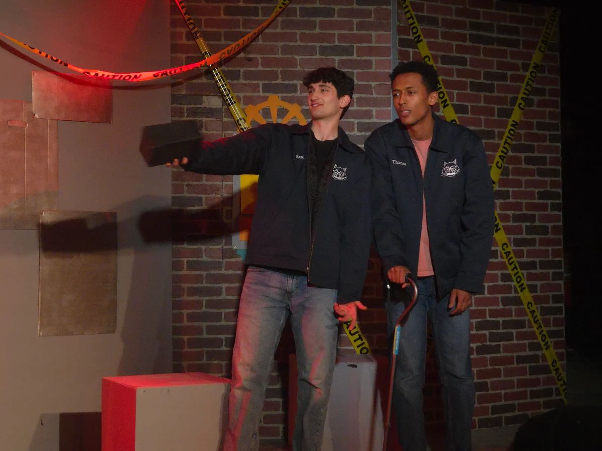 Two performers in blue jackets point off camera to the left.
