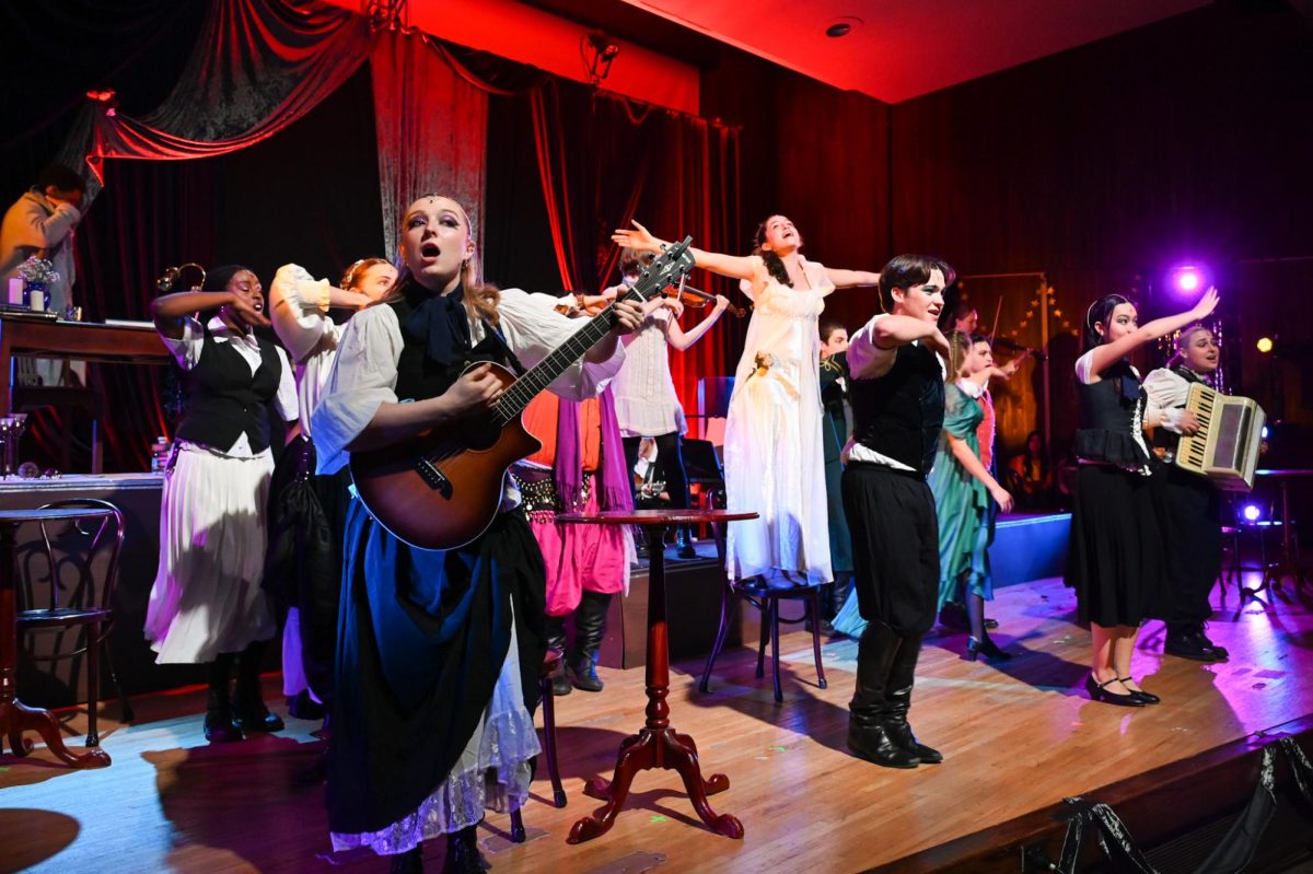 Actors dance and play instruments while facing the audience.