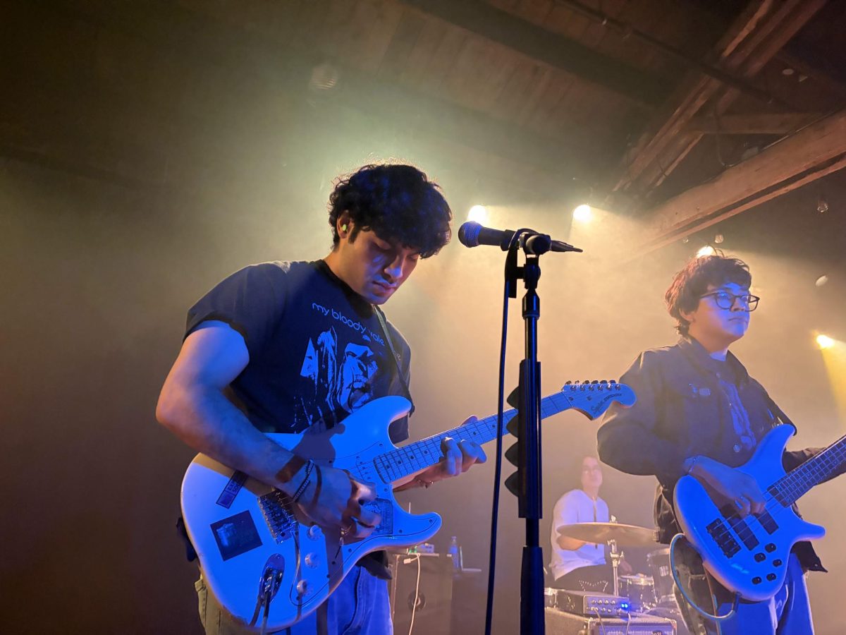 Two members of a band play guitars as light surrounds their heads.