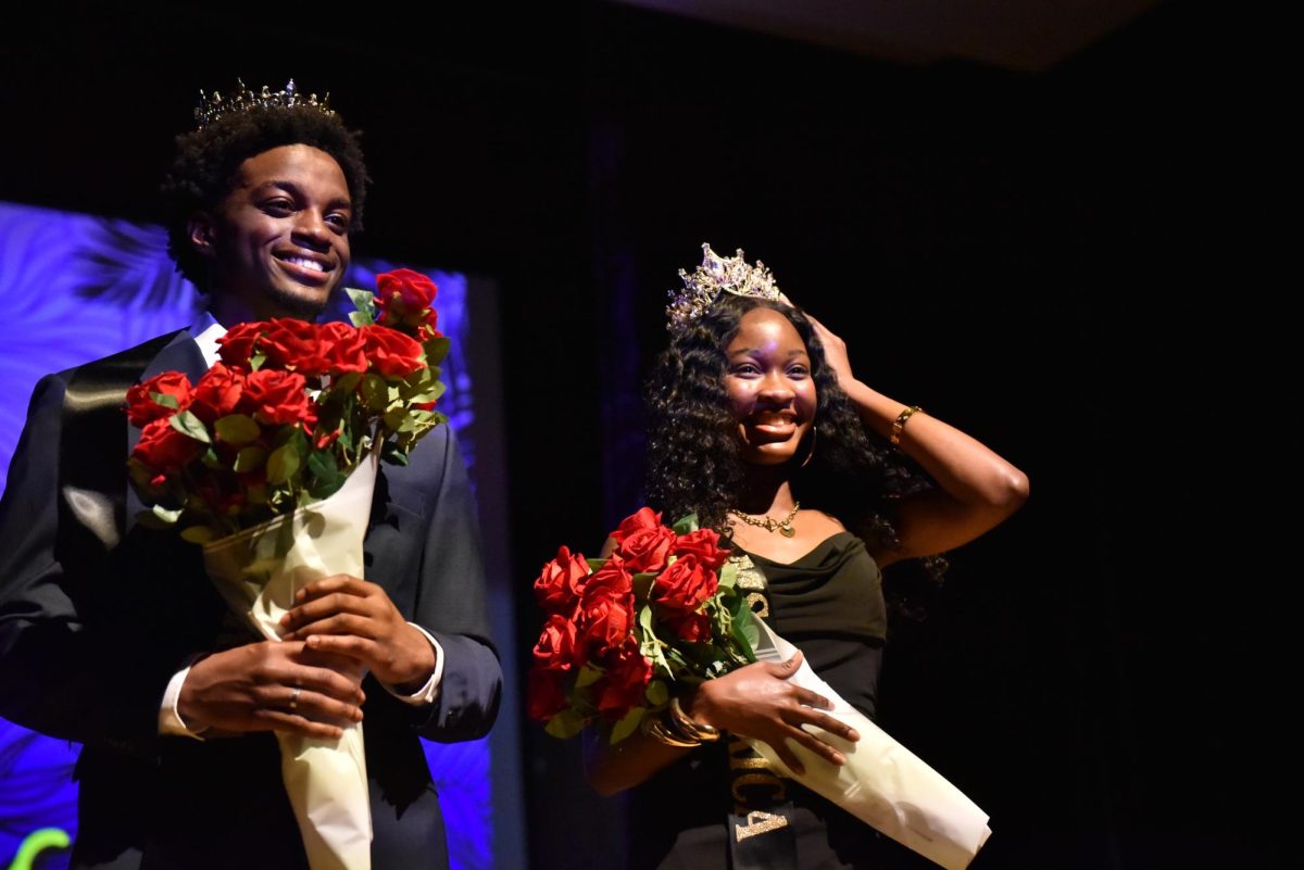 Two students announced Mr. and Ms. Africa with sashes, crowns and roses standing on top of a stage looking at the audience.