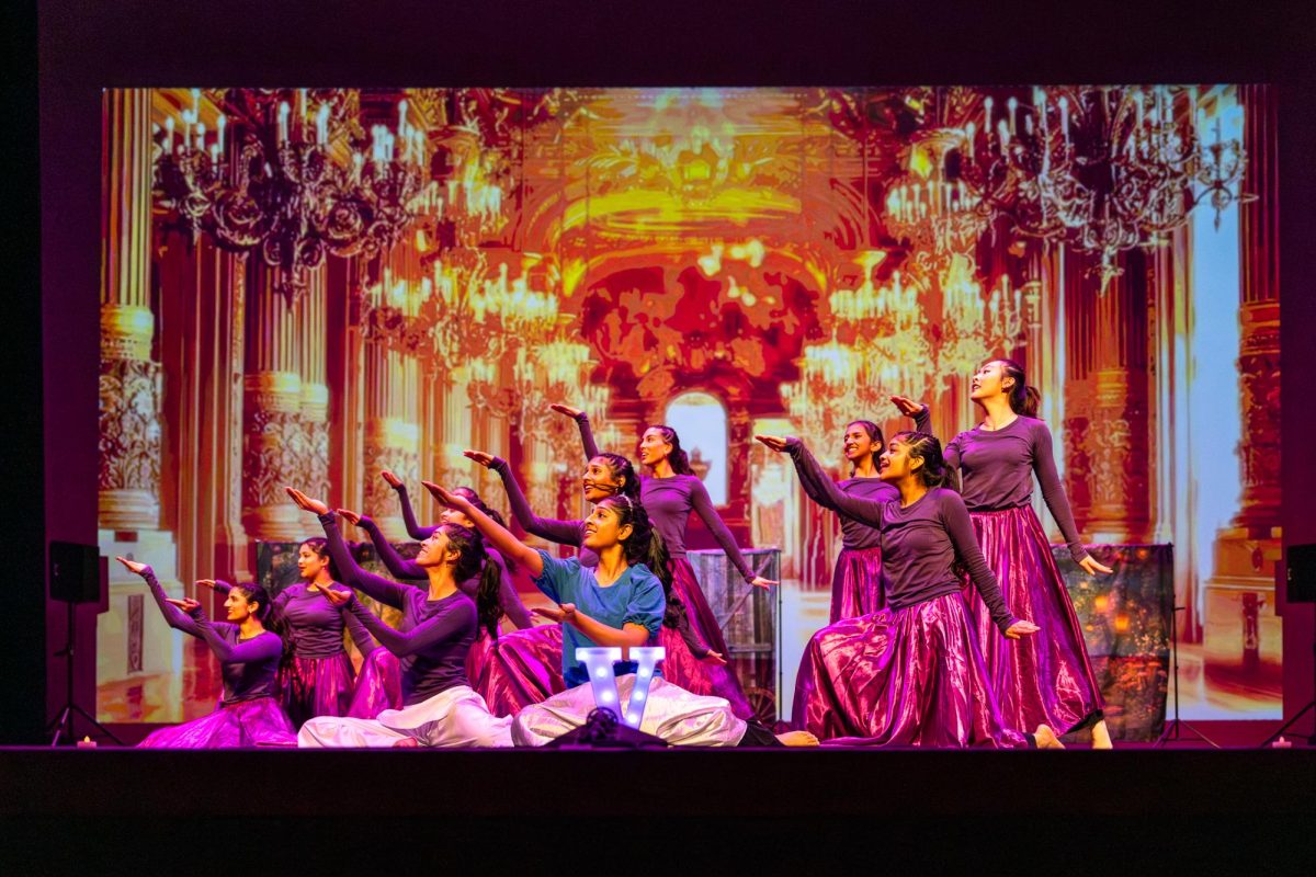 A group of dancers, some sitting and some standing, pose on stage.