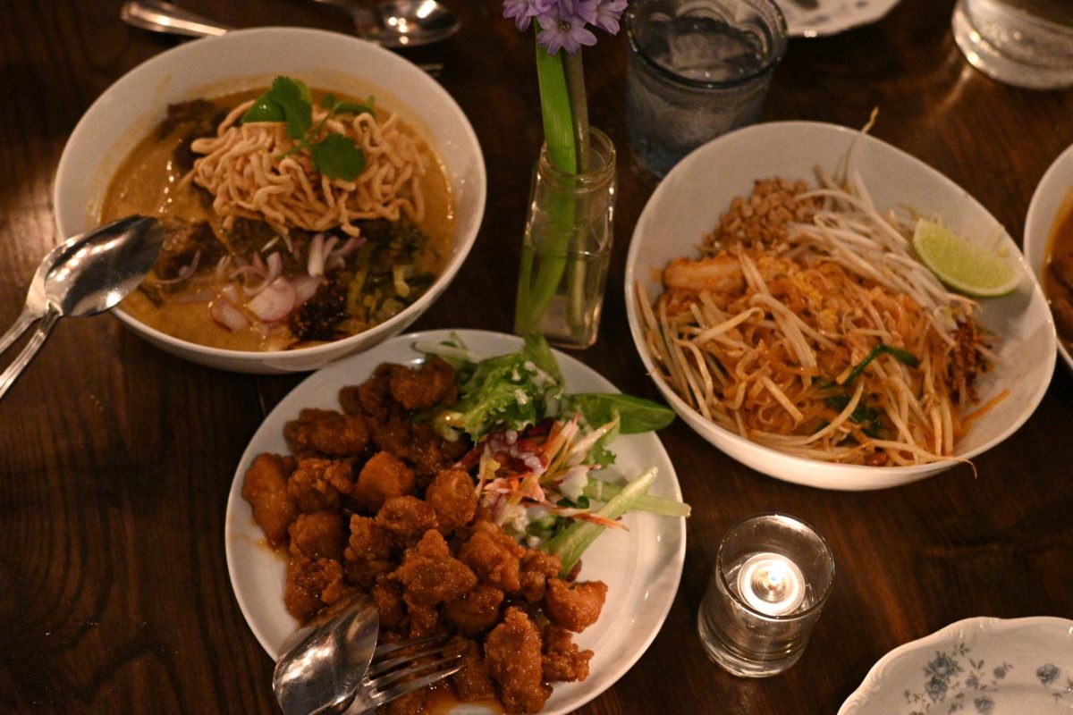 Plates of beef noodles, popcorn chicken and sauteed rice noodles on a table next to a candle.
