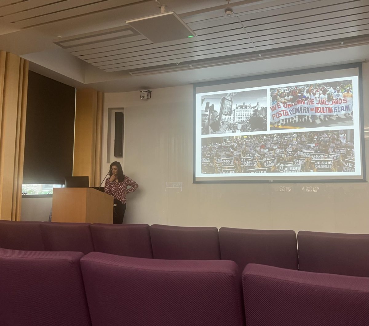 A person stands at a podium in front of a screen.