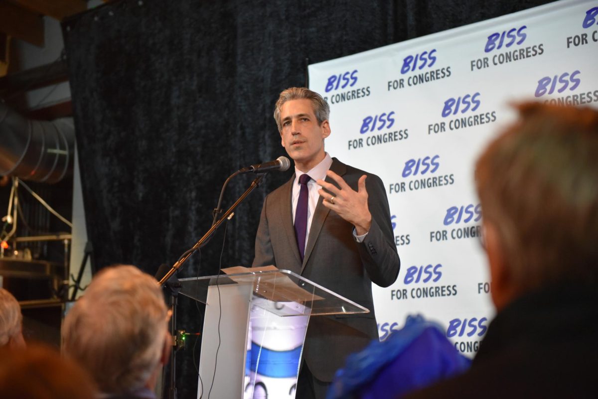 A person speaks into a microphone before a banner with a "Biss for Congress" for congress.