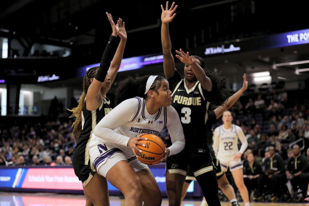 A player in a white jersey holds a basketball, defended by two people in black jerseys.