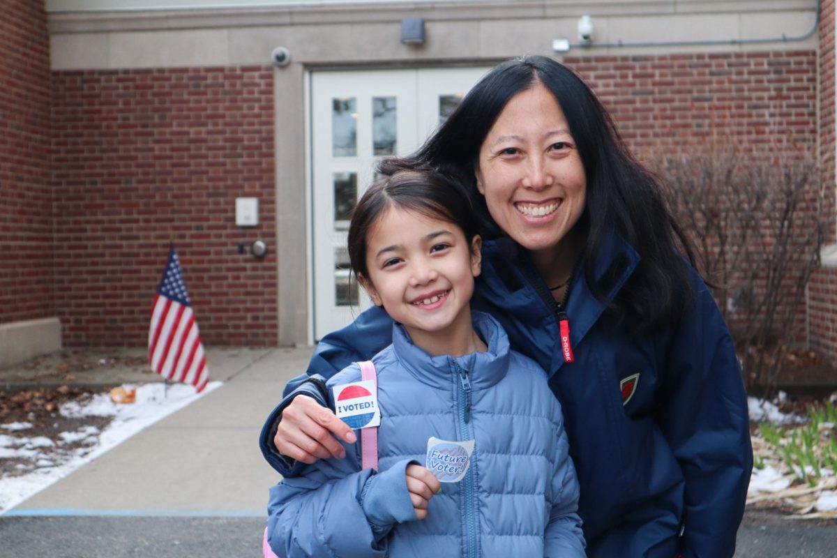 Two people smile at the camera, holding up &ldquo;I voted!&rdquo; stickers.