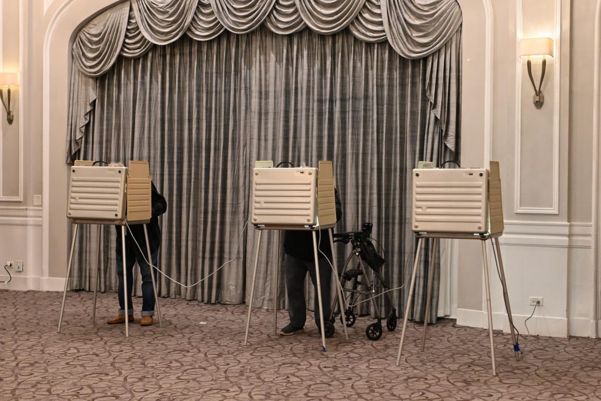 Two people stand hunched over voting booths, their upper bodies hidden by the barriers.