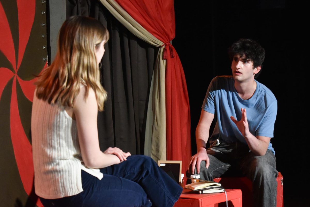 A performer gestures while speaking to someone sitting across from them.