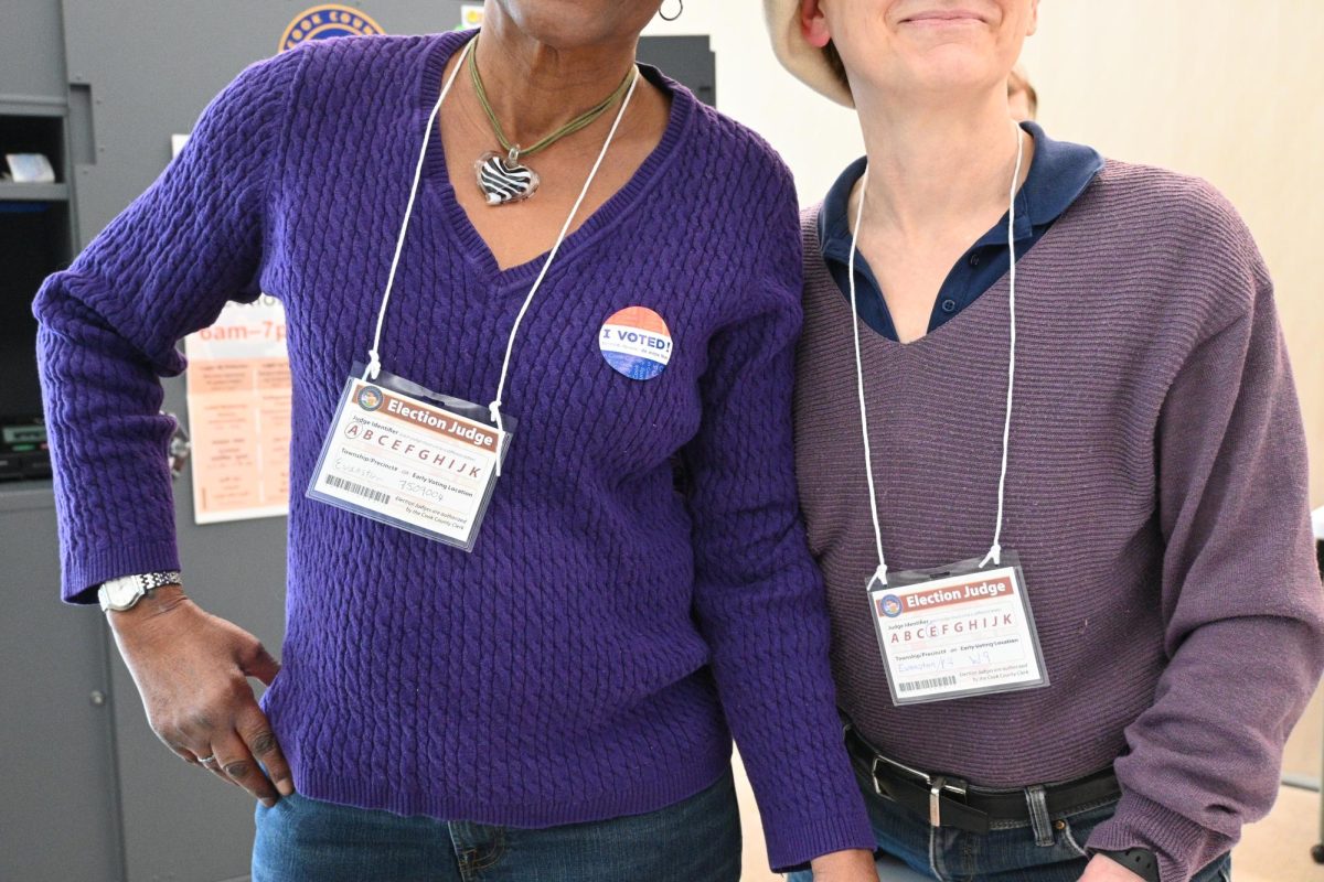 Two people smile at the camera, wearing &ldquo;Election Judge&rdquo; nametags.