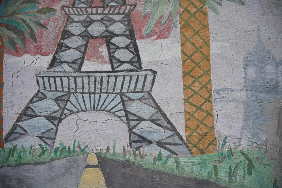 A cracked mural on a wall, featuring the Eiffel Tower and a palm tree.
