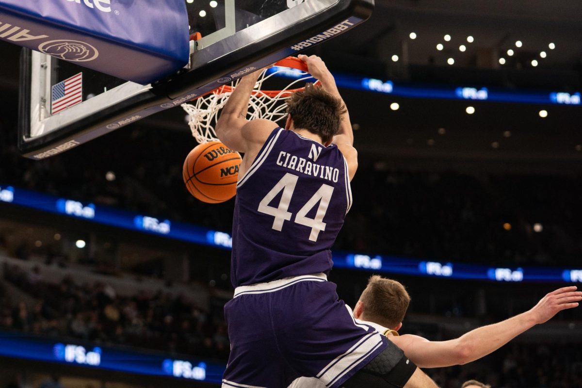 A player in a purple jersey dunks on a player in a white jersey.