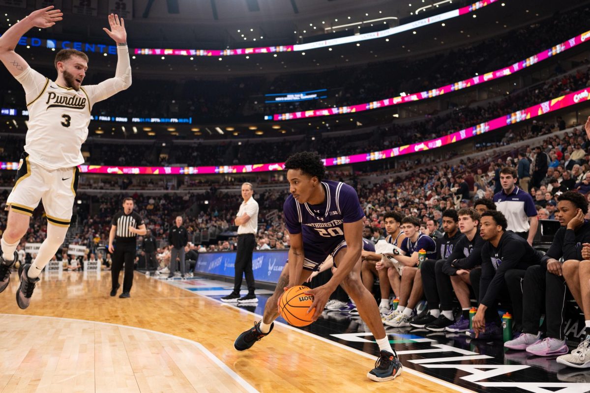 A player in a purple jersey holds the ball while a defender jumps at them.