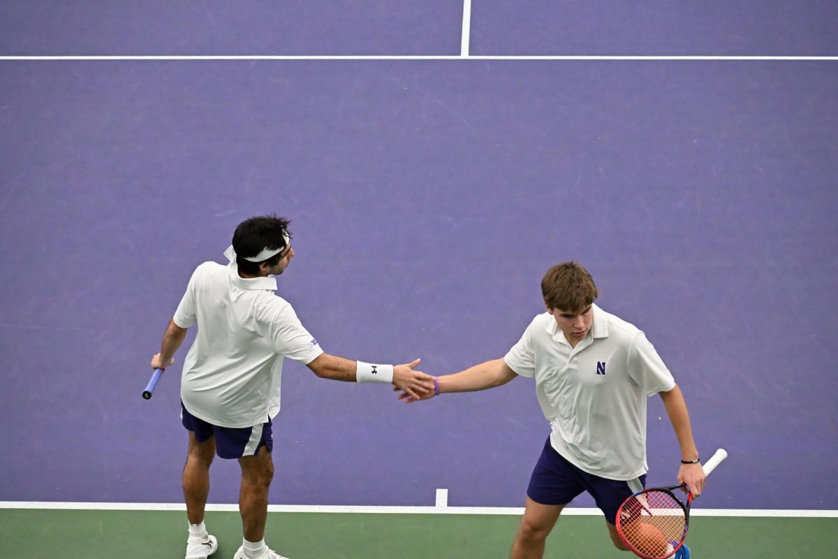 Two people in white shirts, holding tennis rackets high five.