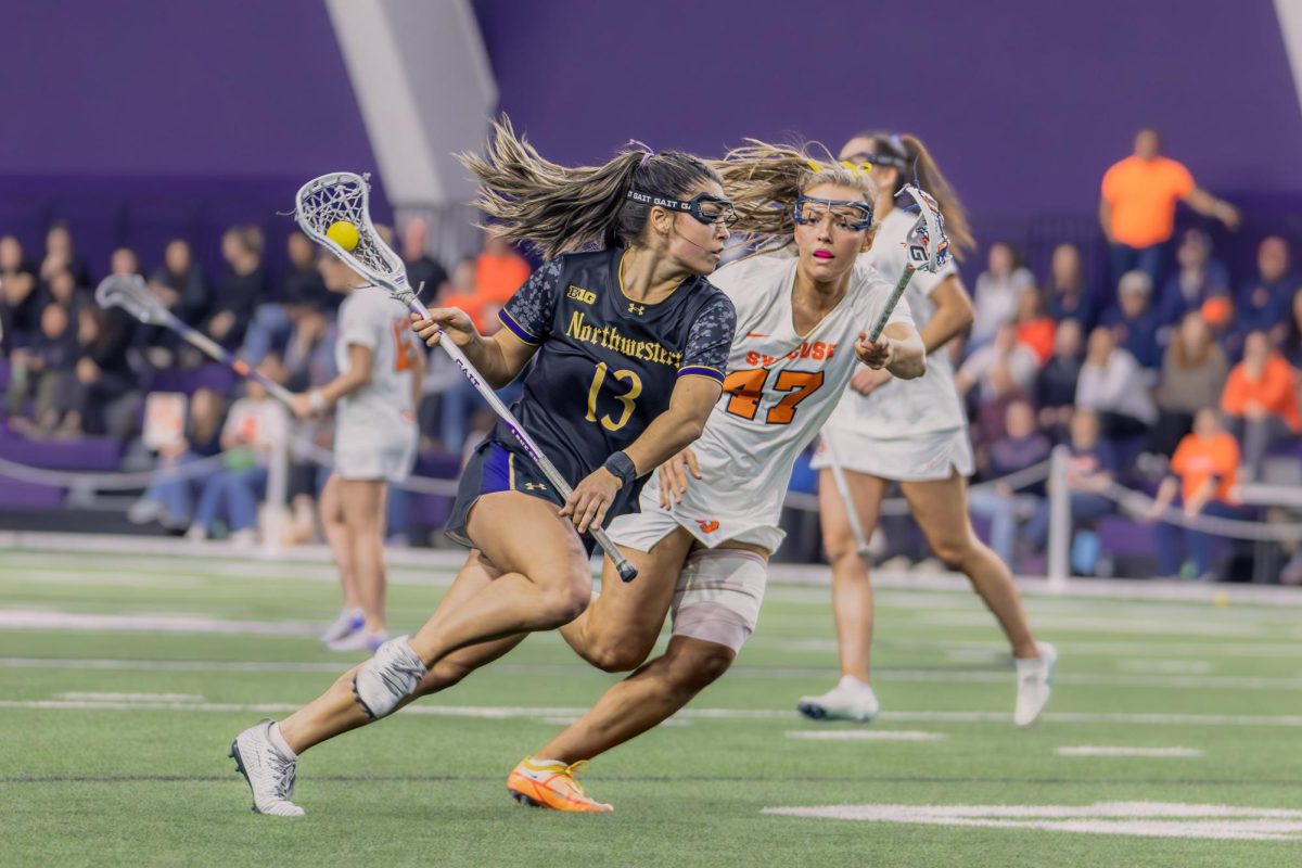 A Northwestern player sprints past a defender while guarding their stick.