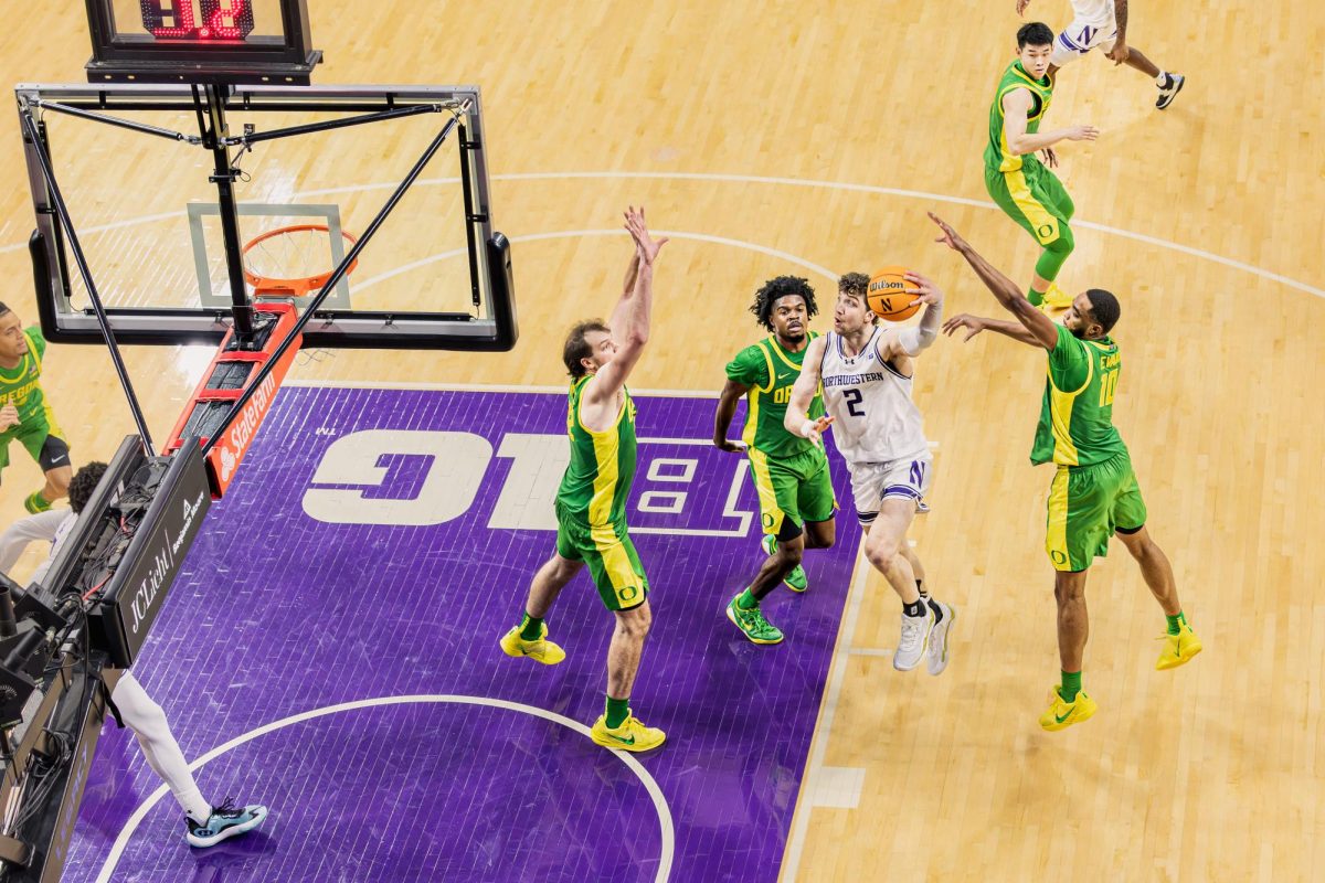 A Northwestern player lays up a hook shot between two defenders in green.