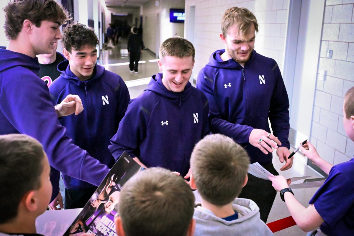 Three men in purple jackets sign autographs for a group of children.