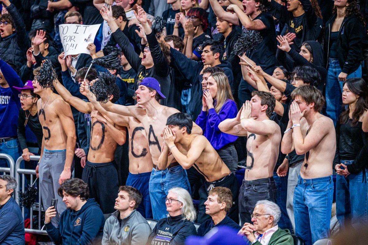 A line of shirtless fans with &ldquo;GO CATS! Painted across their chest cheer.&rdquo;