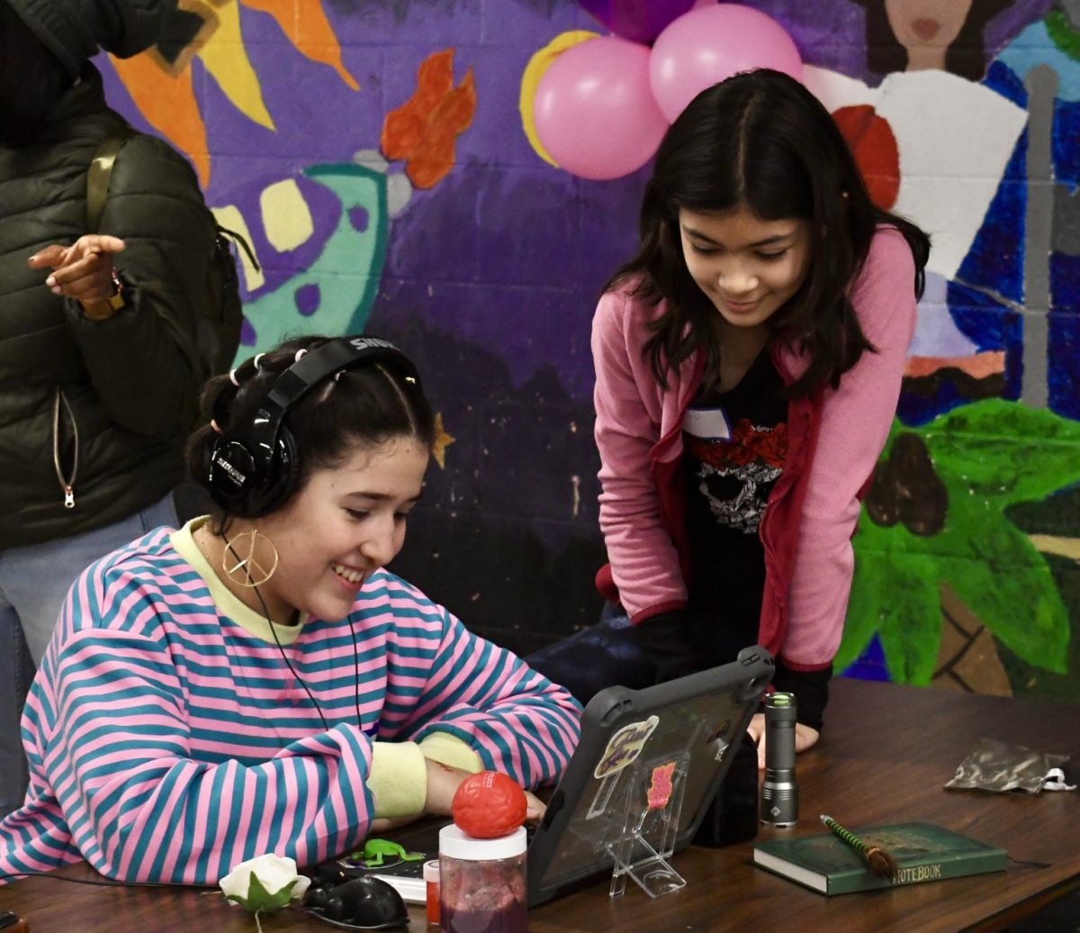 Two girls laugh while working on a laptop.