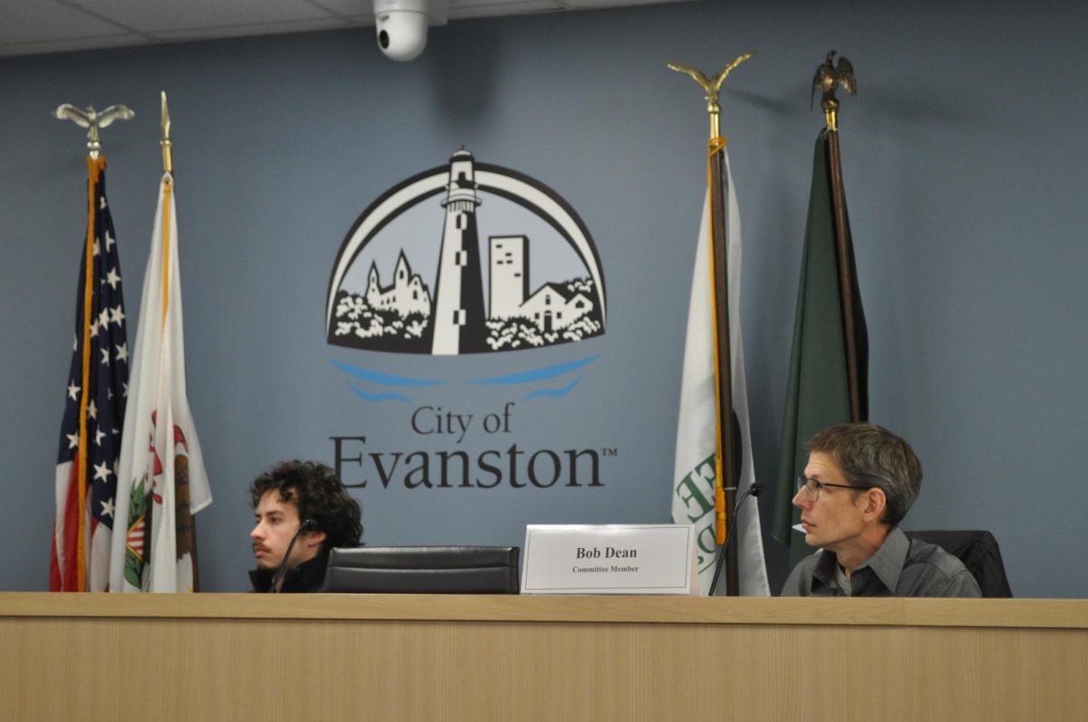 Two people sit in front of the City of Evanston logo.