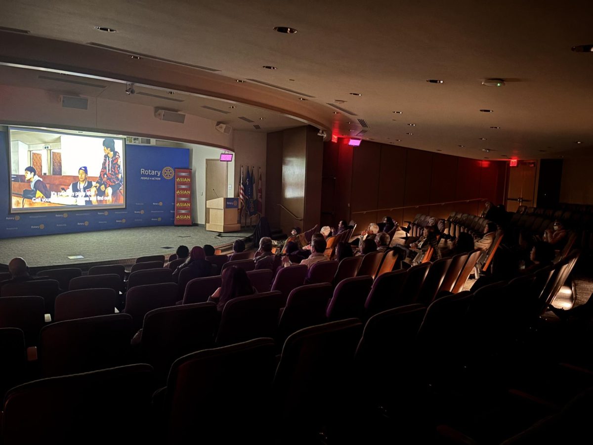 People sitting in an auditorium in One Rotary Center watching the film “Survival Family.”