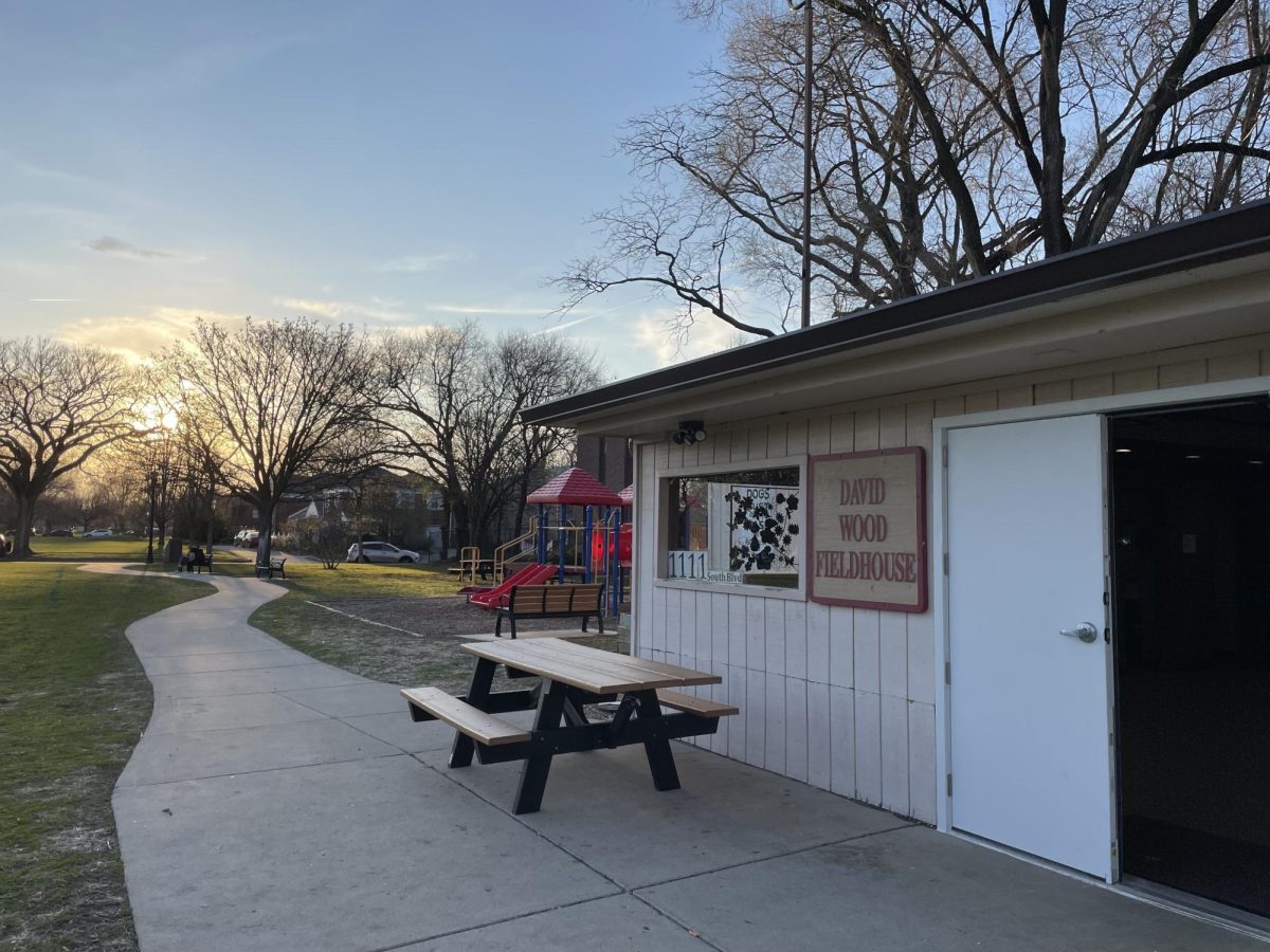 The exterior of a field house with a winding sidewalk and a playground in the distance.