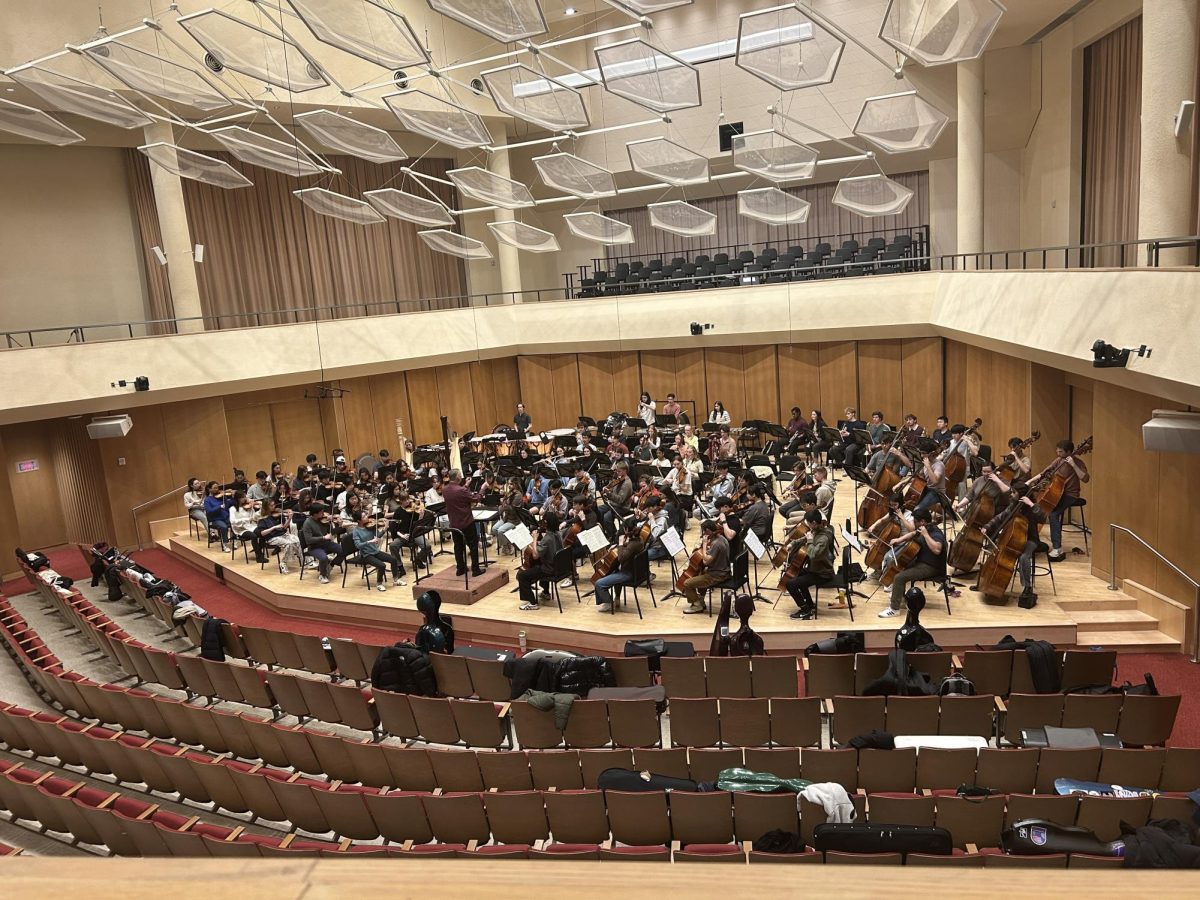 Students rehearsing music in a large, wood-paneled room.