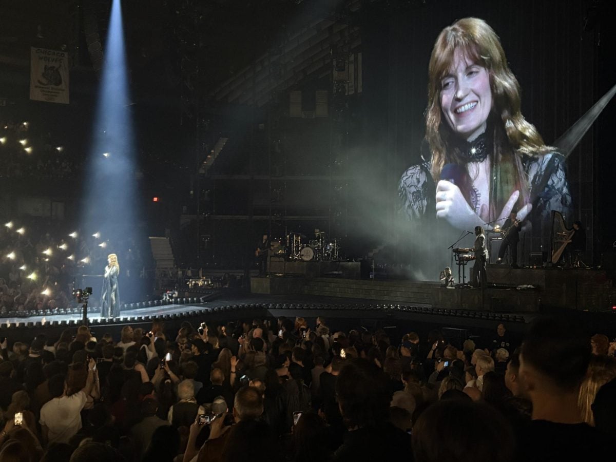 Singer stands on a catwalk. Their face is projected on a large screen above.