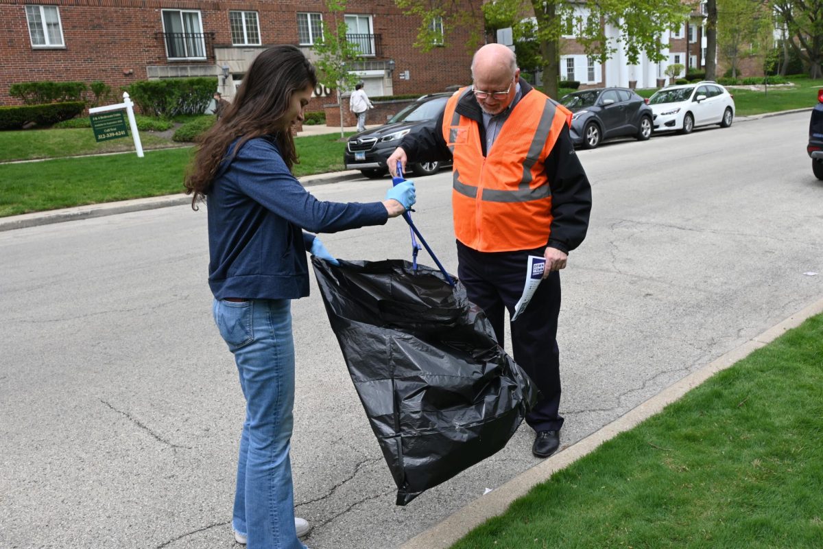 Two people putting trash into a bag using trash grabbers on the street.