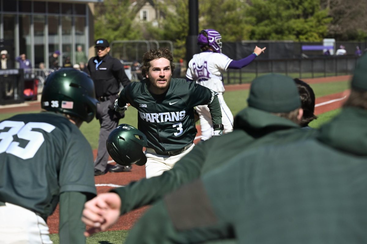 Michigan State batter smiles at their teammates and throws off their helmet in celebration.
