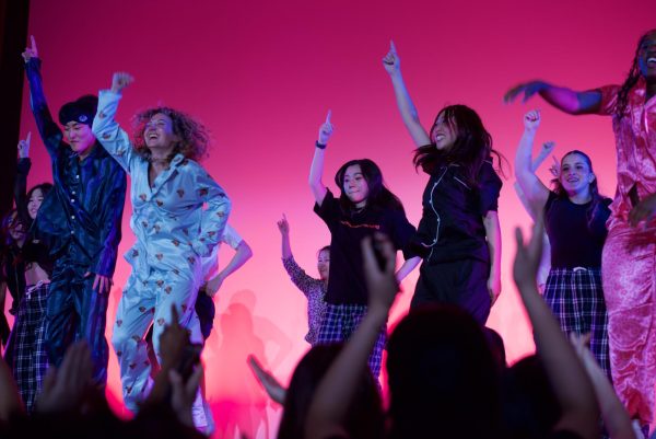 Dancers in pajamas jumping and raising their arms in front of a pink background.