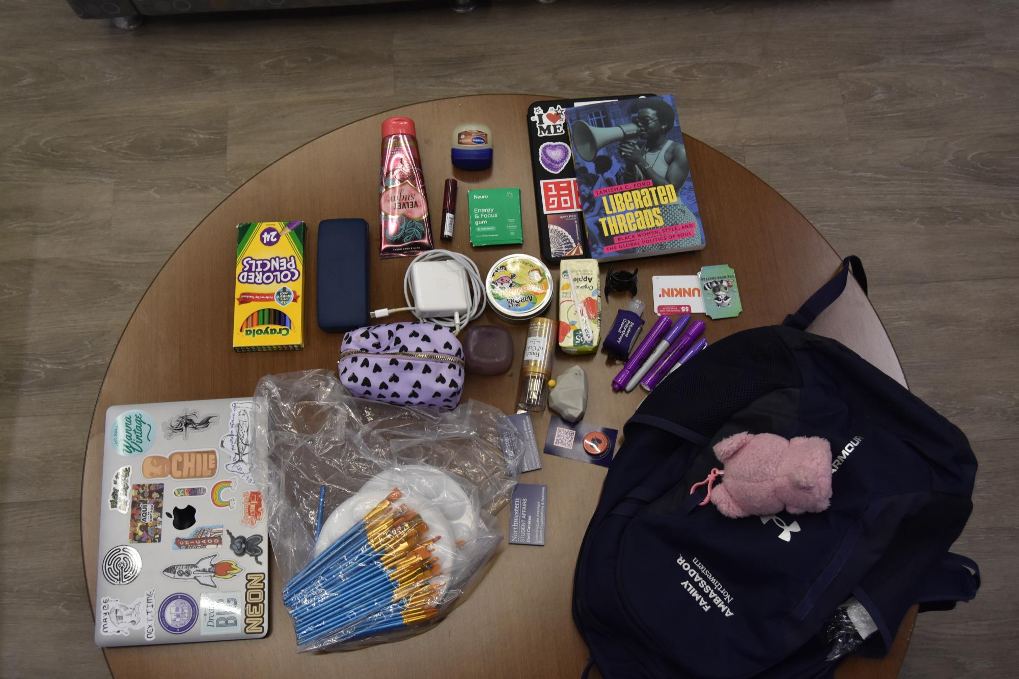 A blue backpack and an assortment of items of a variety of colors is laid out on a brown table.