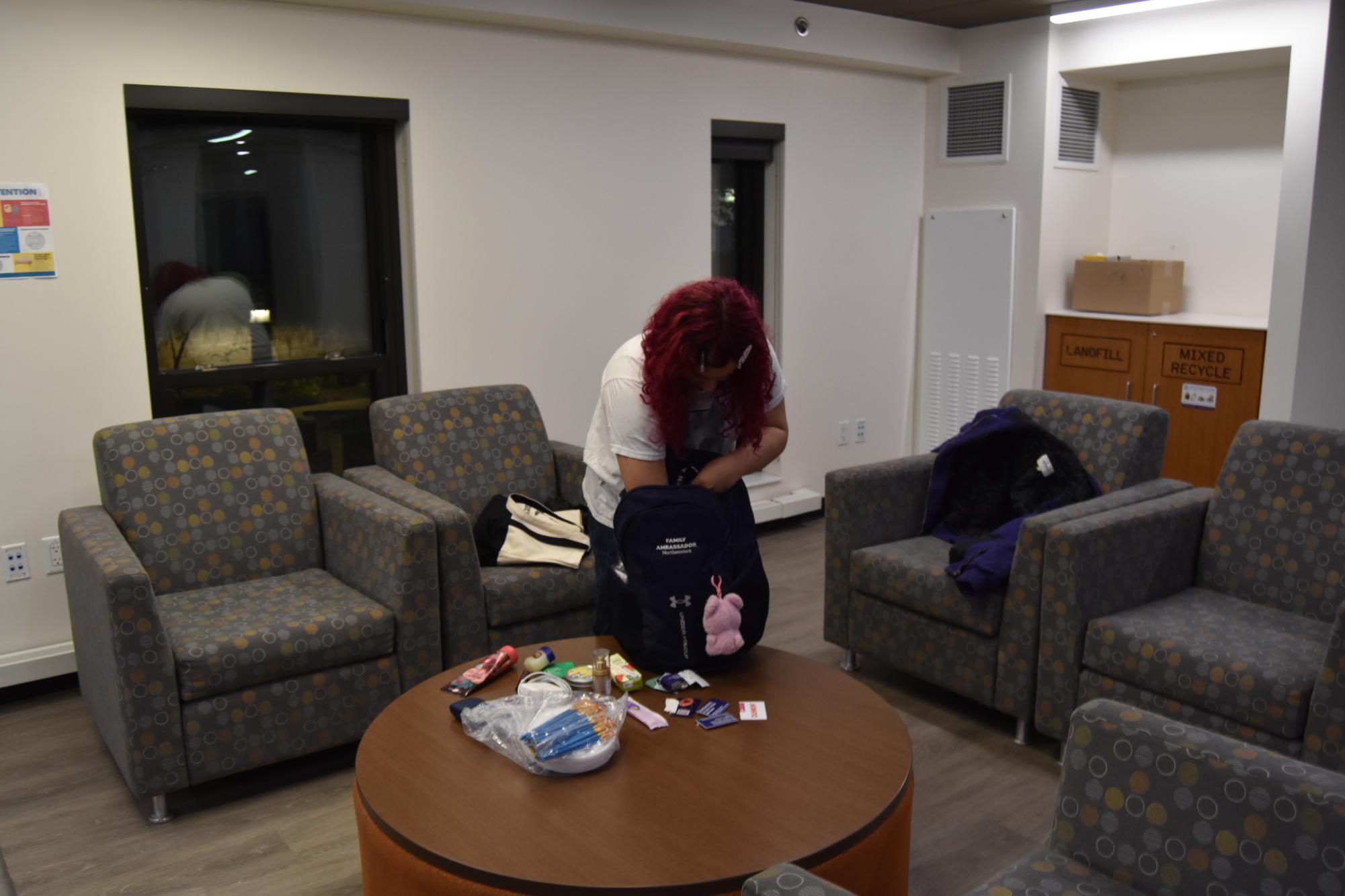 A person with pink hair and a white shirt takes things out of their bag.