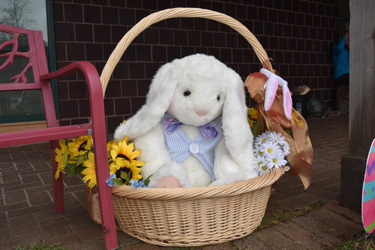 A white bunny stuffed animal sat in a wicker basket with flowers.