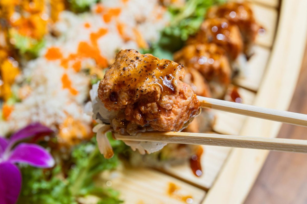 A pair of chopsticks holds a sex on the beach roll to showcase the unagi sauce and salmon on top.