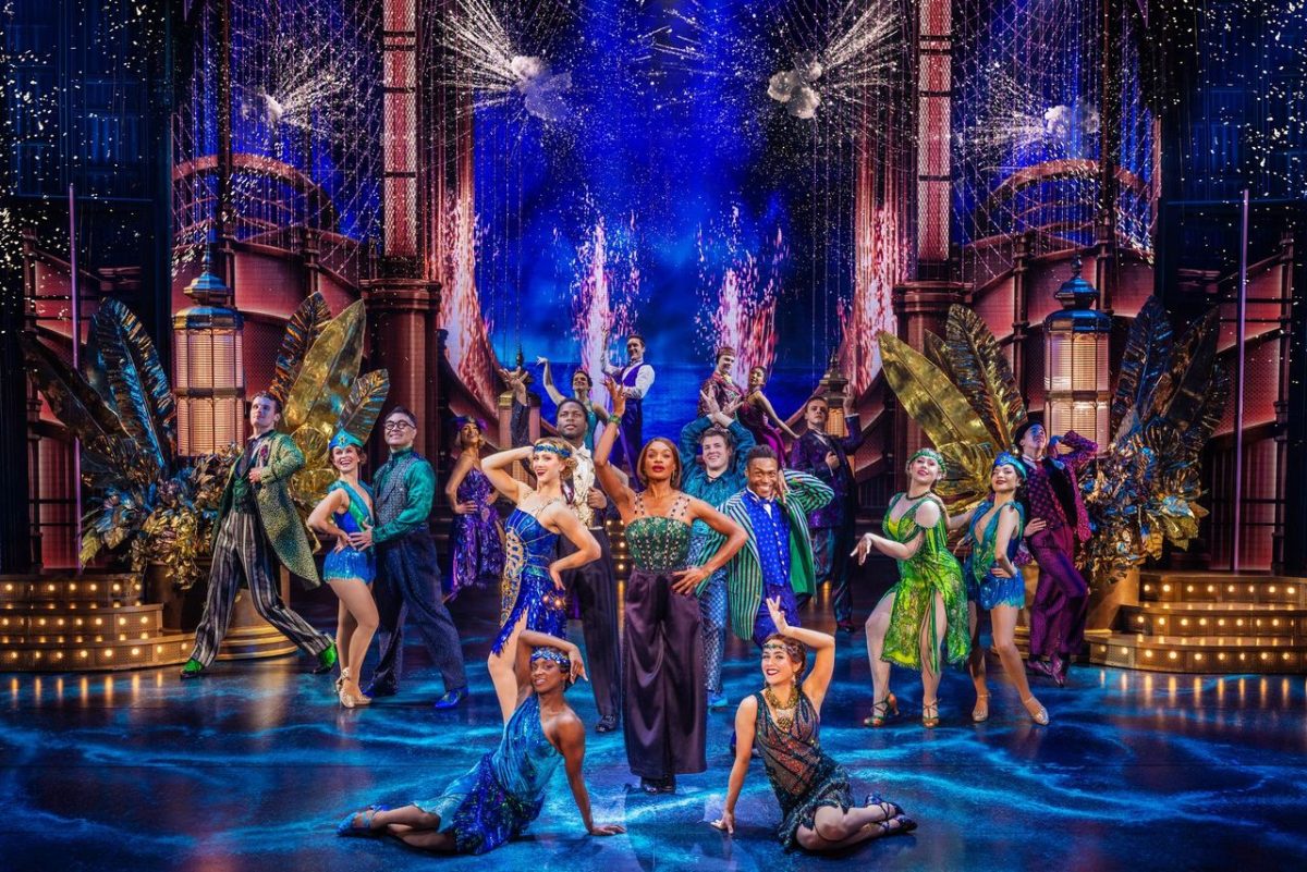 Cast members pose centerstage in a colorful tableau.