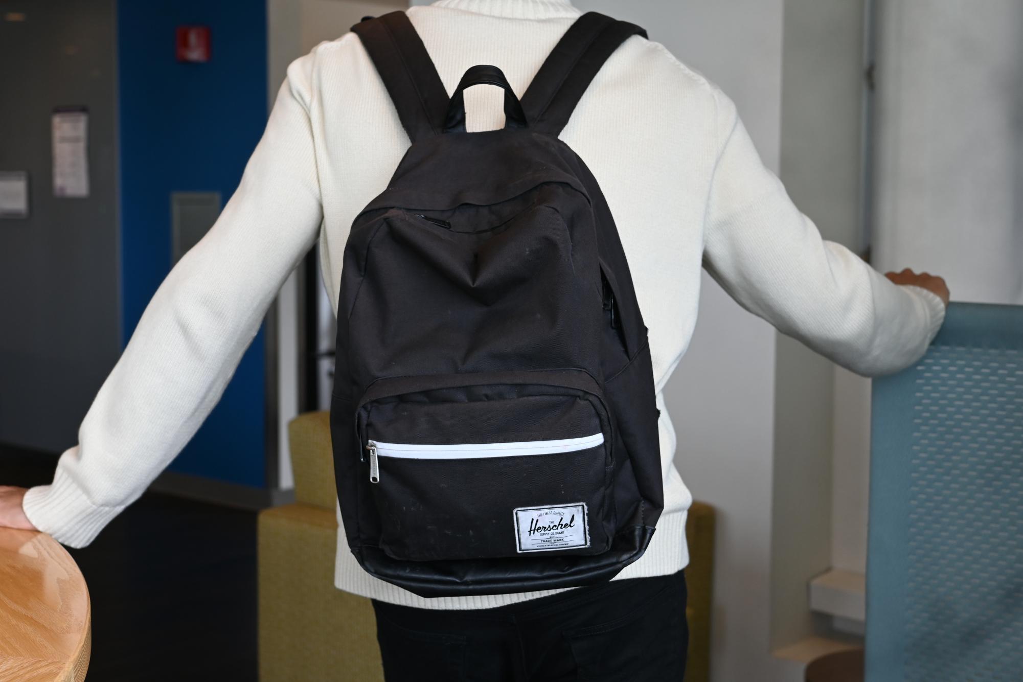 A young man shows his black Herschel backpack inside his dorm building.
