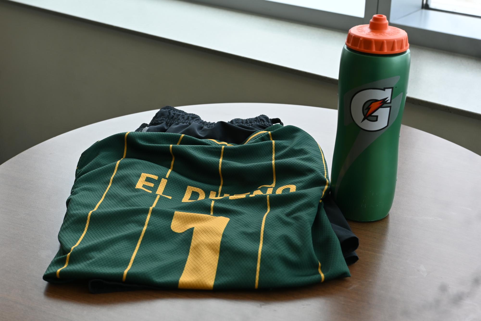 A spread of green and yellow soccer jersey, black shorts and a green Gatorade water bottle sits on a wooden table.