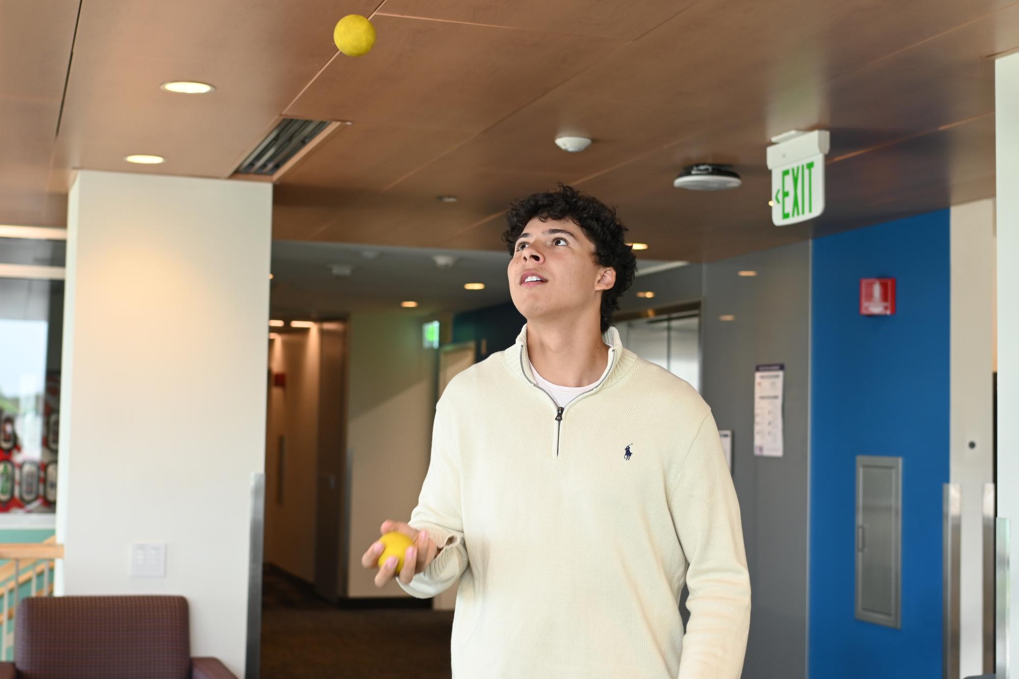 A young man tosses two yellow lacrosse balls into the air.