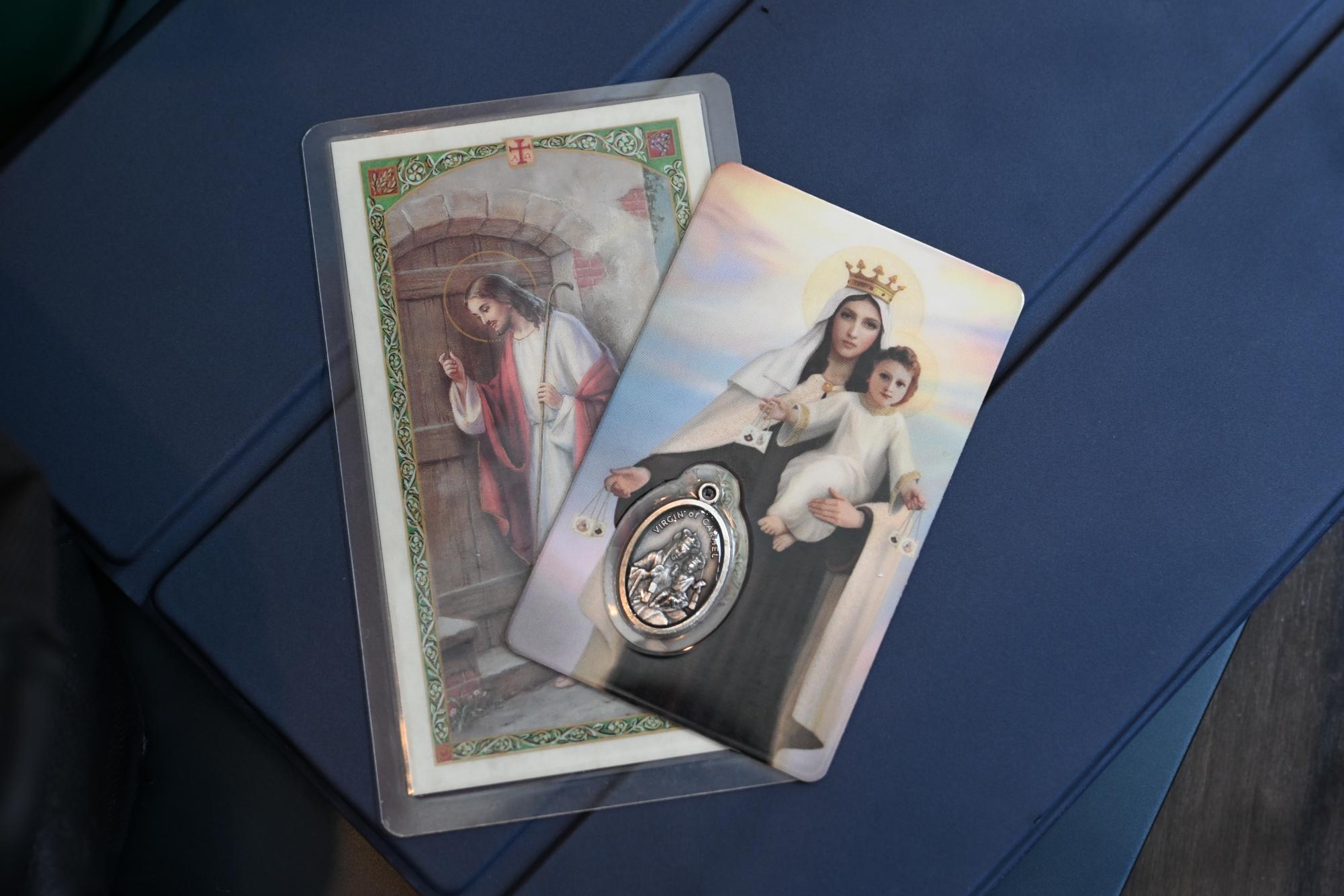 Two prayer cards, one containing a pendant, displayed on top of a blue iPad case.