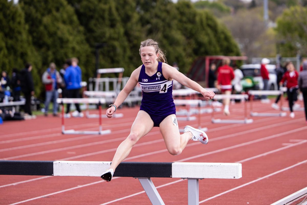 A runner in a purple singlet jumps over a black and white barrier.
