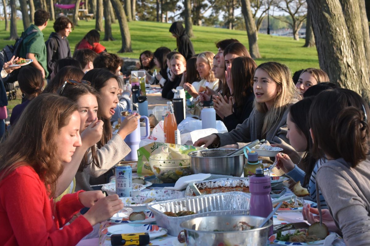 Students sit at a long table, eating and talking.