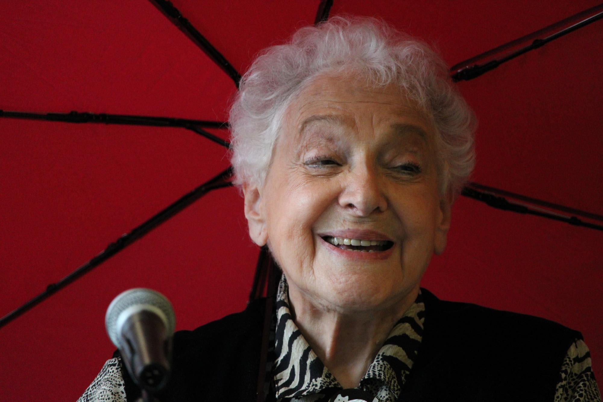 A person smiles with a red umbrella behind them.