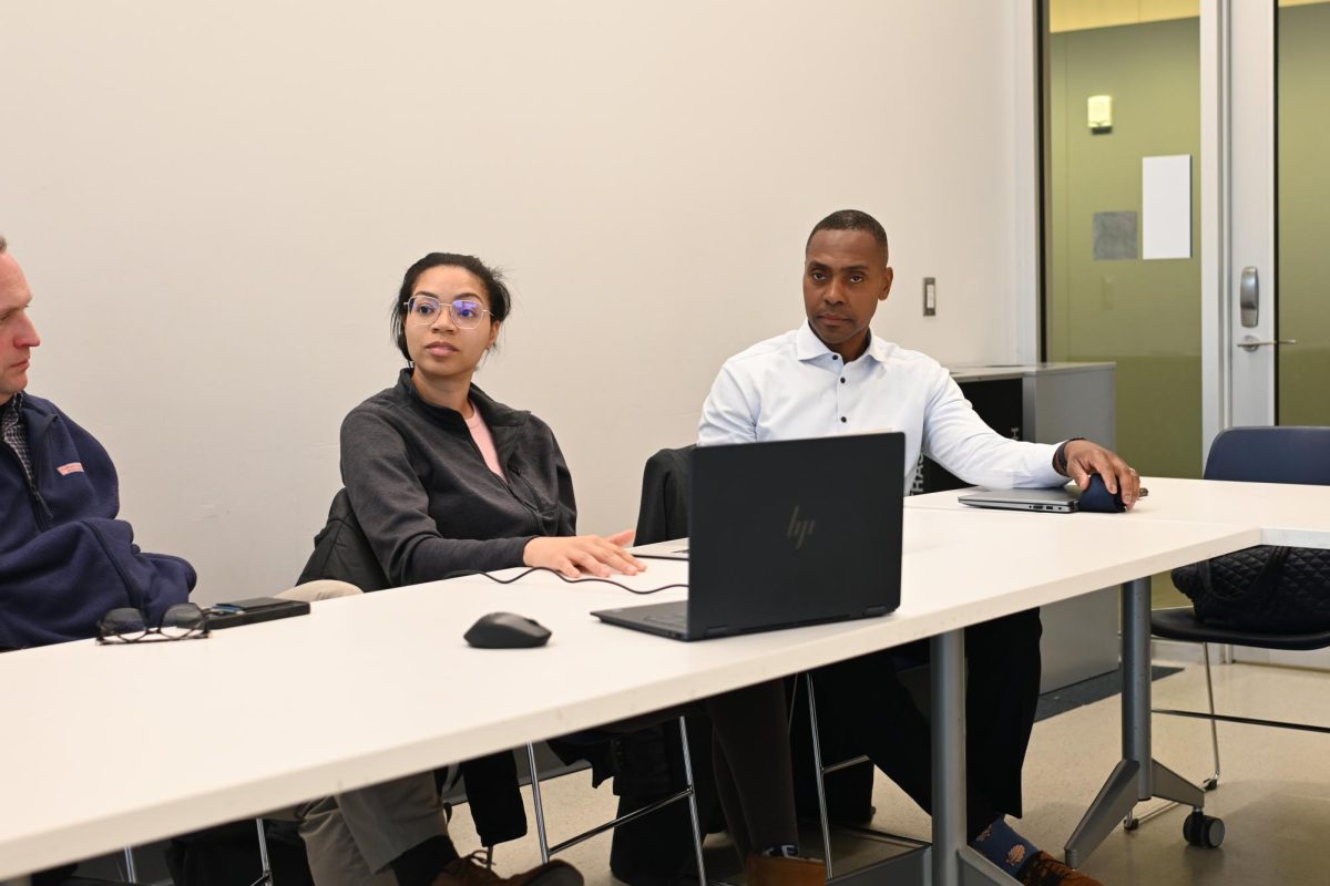 Two people sit behind a desk.