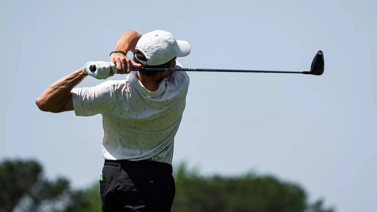 A player wearing white swings a golf club.