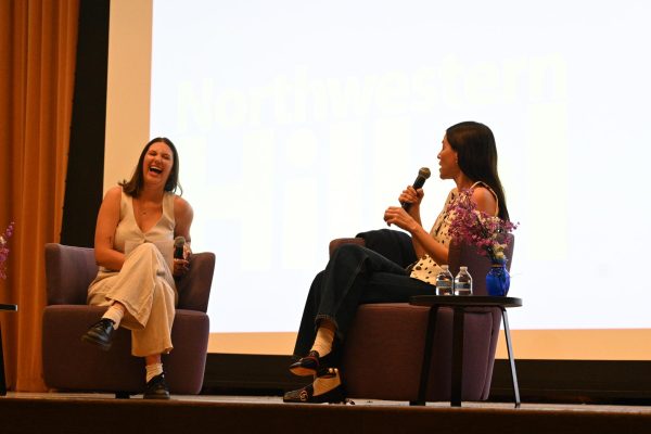 Two people holding microphones, sitting on stage talking.