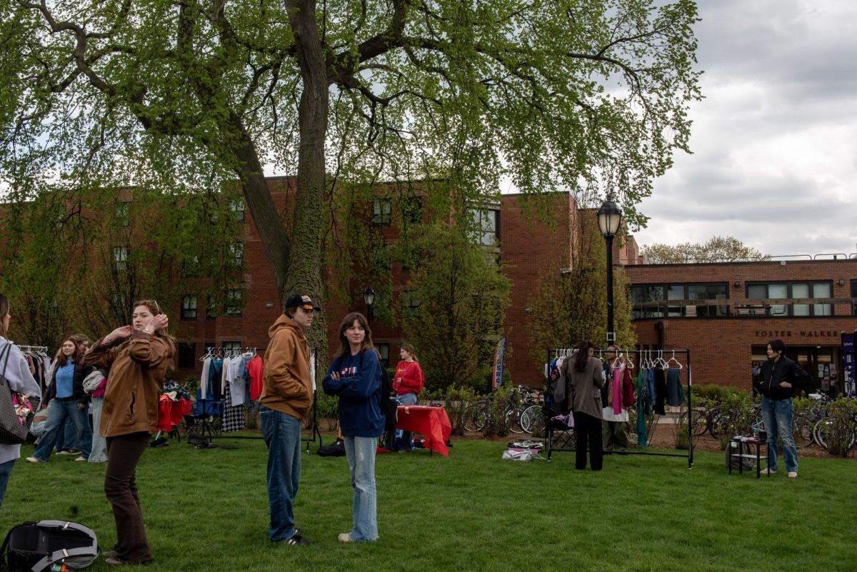  People standing and interacting on a lawn, surrounded by tables and students in the background.